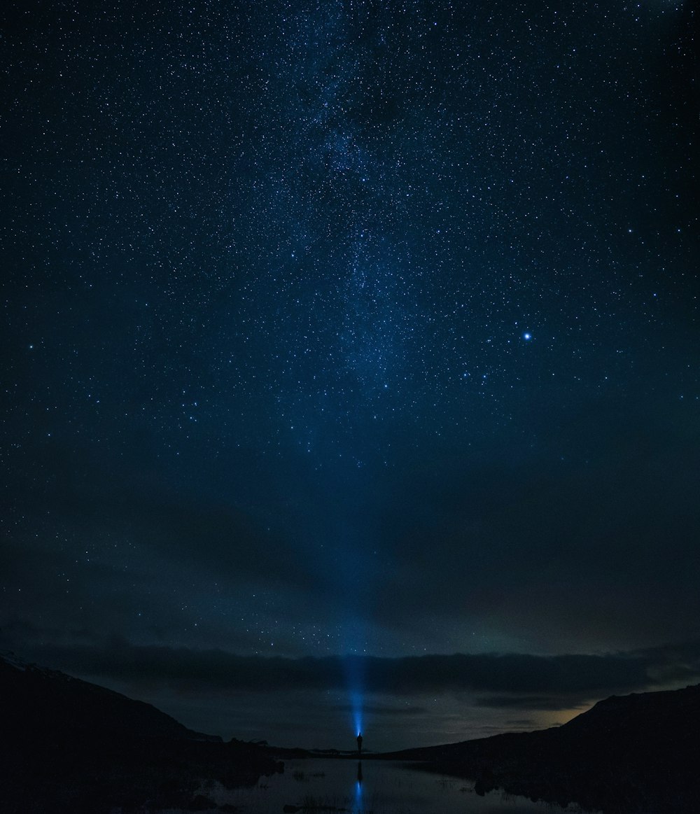 torcia elettrica della luce della persona verso il cielo durante il cielo pieno di stelle