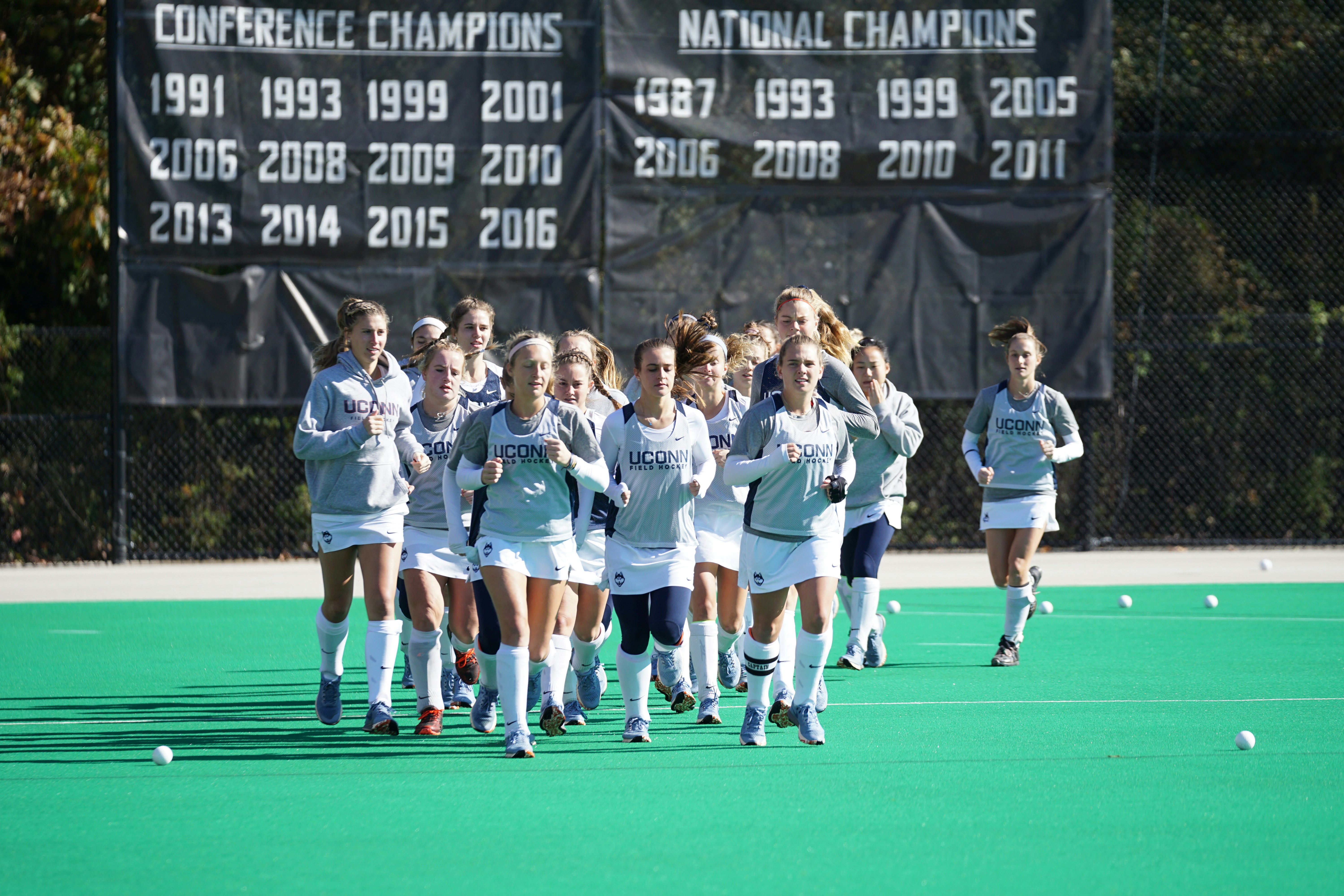 group of women athletes jogging on field field hockey teams background