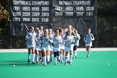 group of women athletes jogging on field field hockey teams background