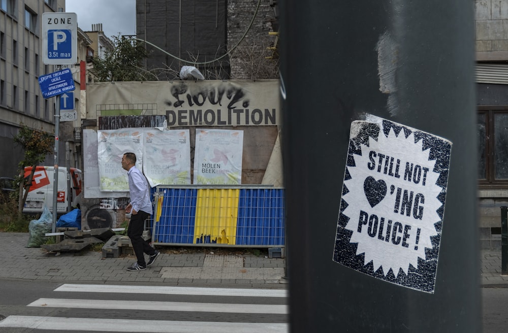 still not loving' police sticker stamped on pole overlooking person standing beside pedestrian lane at daytime