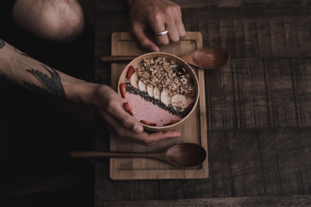 person holding cooked dish inside bowl beside brown wooden spoon