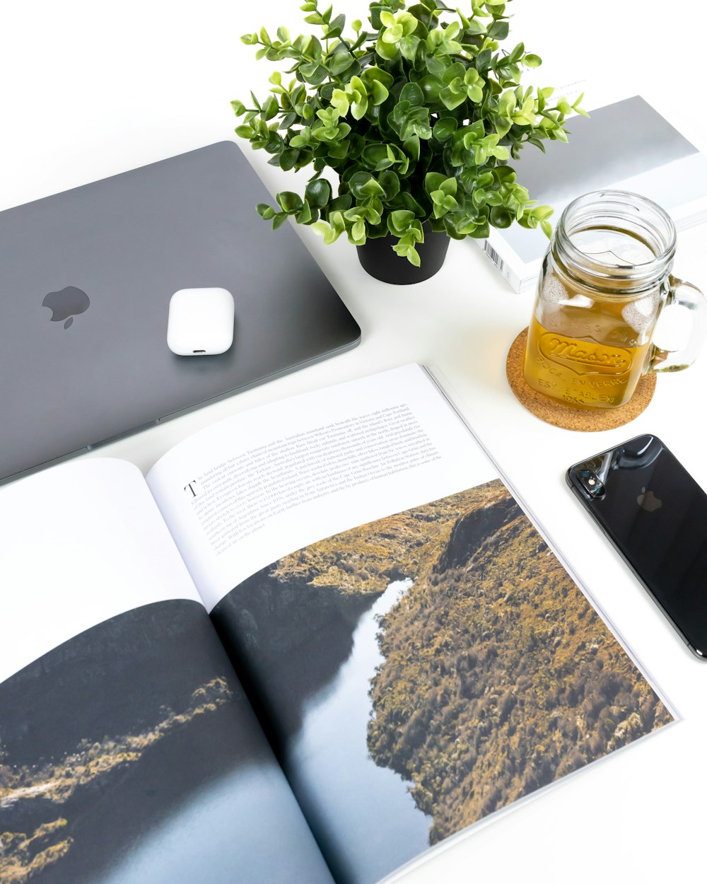 緑の葉の植物、MacBook、スペースグレイのiPhone Xのそばに半分空の透明なガラス瓶