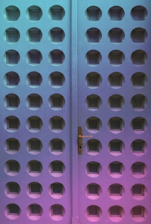 A door with a unique design featuring a grid of circular indents. The door handle is visible on the right panel, and the surface displays a gradient of colors ranging from teal to pink.