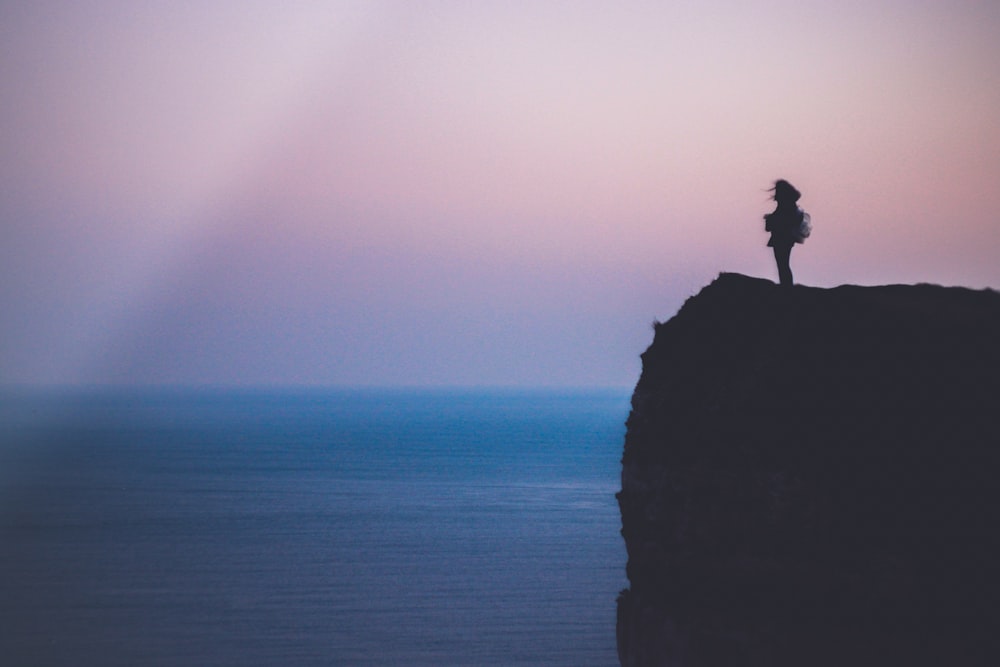 silhouette de personne debout sur la falaise de la mer pendant l’heure d’or