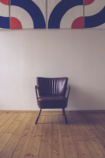 An elegant black leather chair against a dark gray wall with a silver-framed abstract painting.