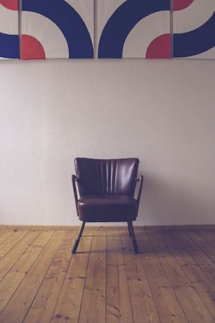 An elegant black leather chair against a dark gray wall with a silver-framed abstract painting.