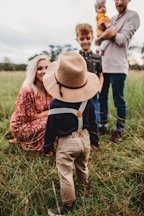 woman sitting on grass while facing boy in brown hat