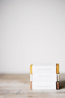 Elegant display of soap bars wrapped in cream-colored paper with sage green ribbons on an asymmetric wooden shelf.