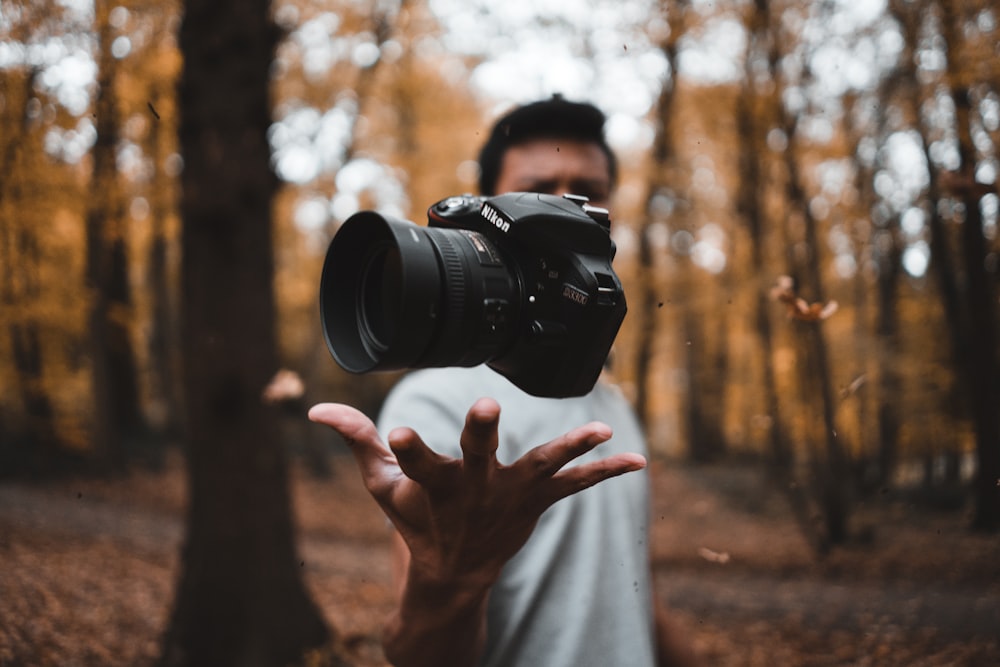 森で男の手の上に浮かぶ黒いデジタル一眼レフカメラ