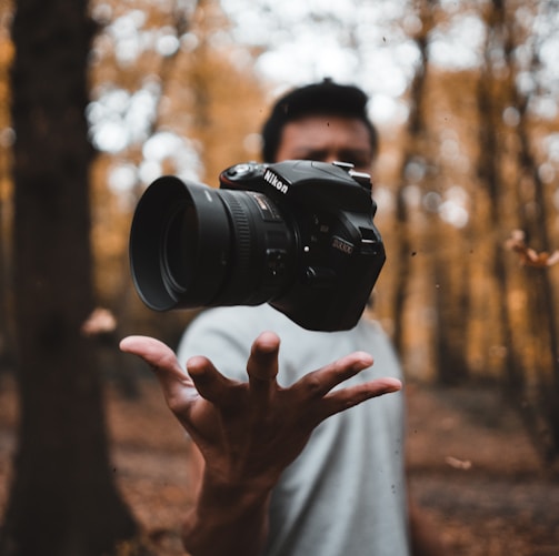 black DSLR camera floating over man's hand at the woods