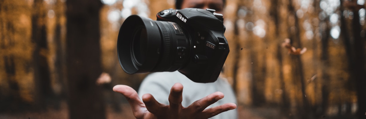 black DSLR camera floating over man's hand at the woods