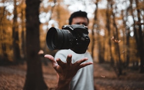 black DSLR camera floating over man's hand at the woods