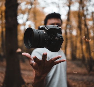 black DSLR camera floating over man's hand at the woods