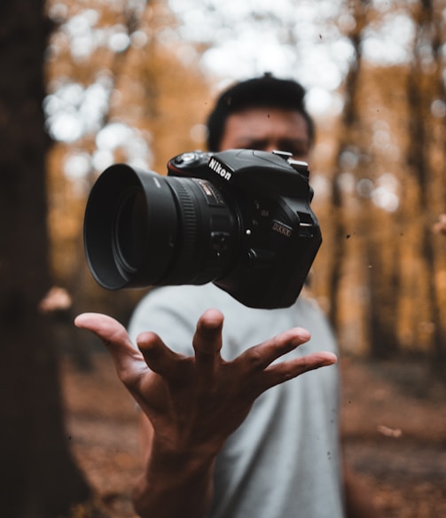 black DSLR camera floating over man's hand at the woods