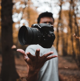 black DSLR camera floating over man's hand at the woods