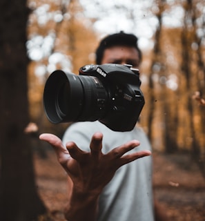 black DSLR camera floating over man's hand at the woods