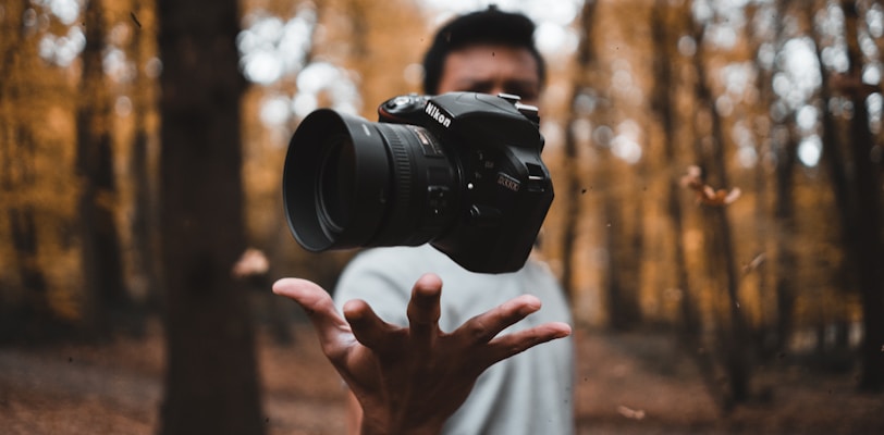 black DSLR camera floating over man's hand at the woods