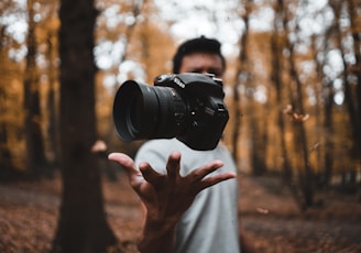 black DSLR camera floating over man's hand at the woods