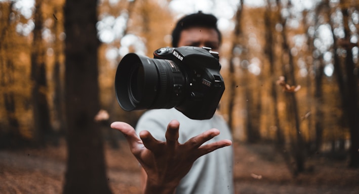 black DSLR camera floating over man's hand at the woods