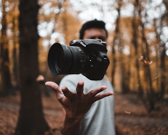 black DSLR camera floating over man's hand at the woods