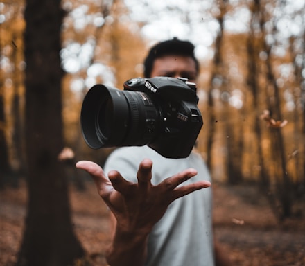 black DSLR camera floating over man's hand at the woods