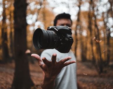 black DSLR camera floating over man's hand at the woods