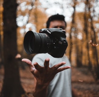 black DSLR camera floating over man's hand at the woods