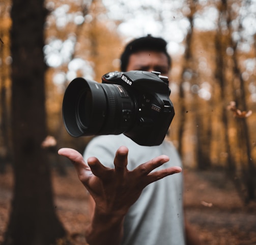 black DSLR camera floating over man's hand at the woods