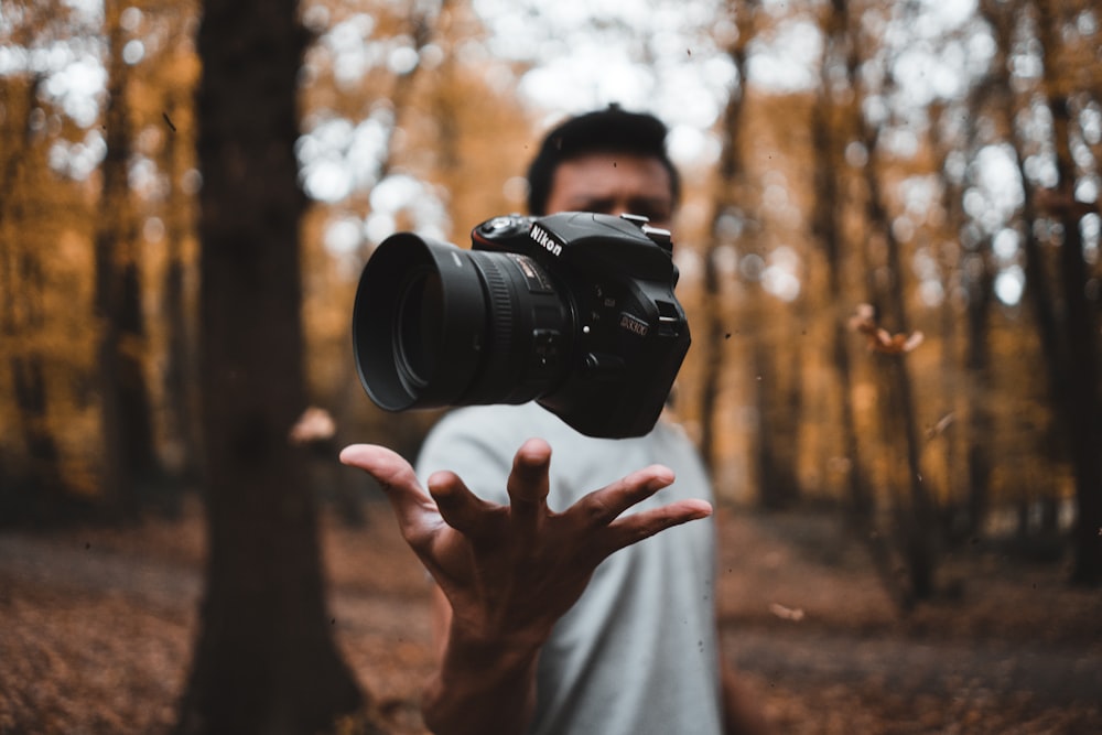 schwarze DSLR-Kamera, die über der Hand eines Mannes im Wald schwebt