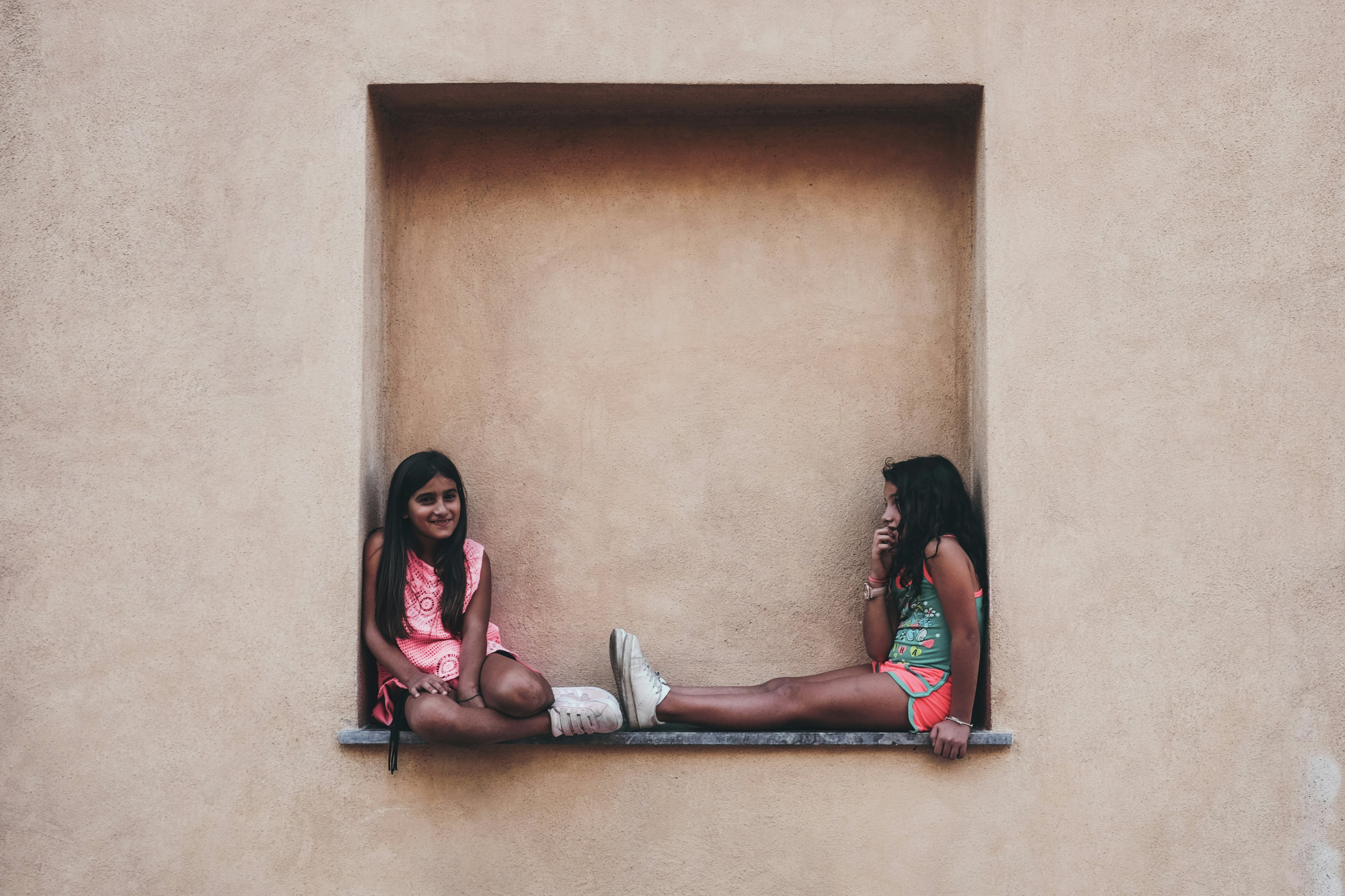 two girl in pink and green shirts sitting on wall shelf