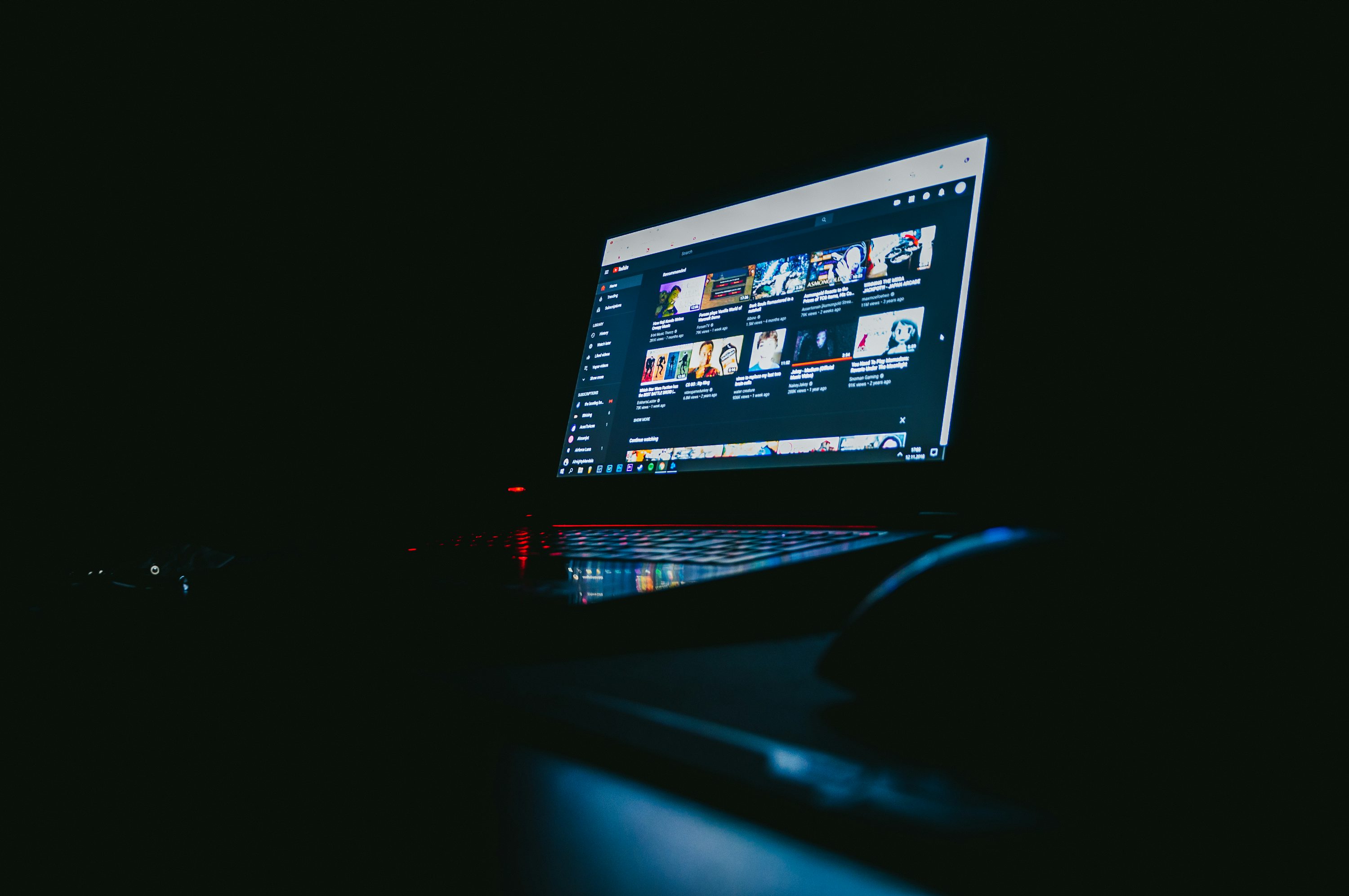 A laptop sits on a desk in the dark, showing YouTube videos about how to get your video suggested on YouTube