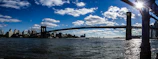 A panoramic view of a completed bridge spanning a wide river under a clear sky.