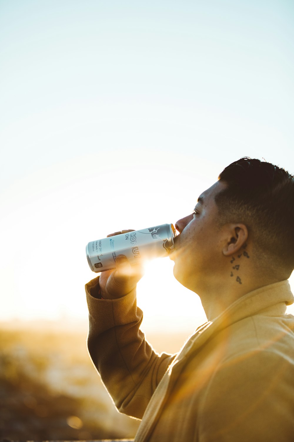 man wearing yellow coat drinking from can