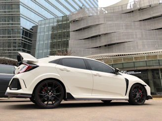 A glossy white car parked in an urban setting featuring a carbon fiber spoiler.