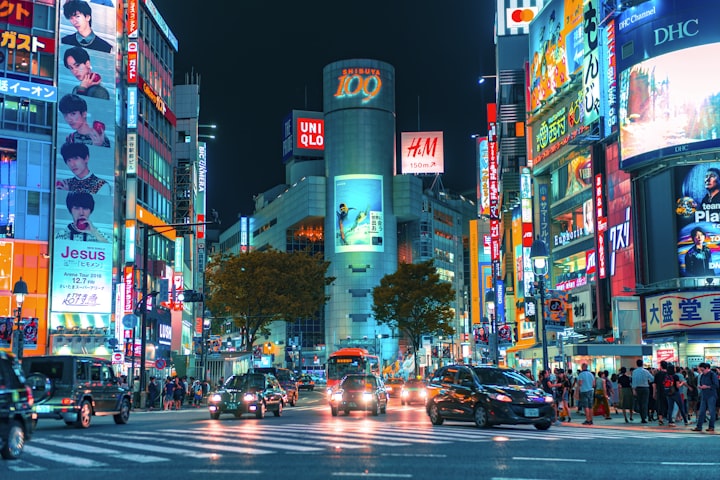 Shibuya crossing at night, traffic and crowds under neon signs
