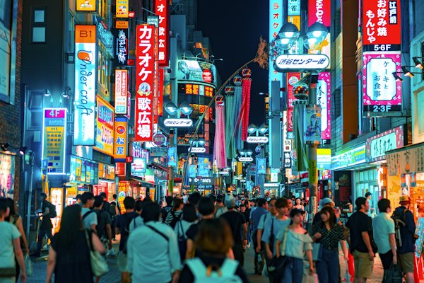 A crowd of people walking down a neon-lit street in Shibuya, Tokyo