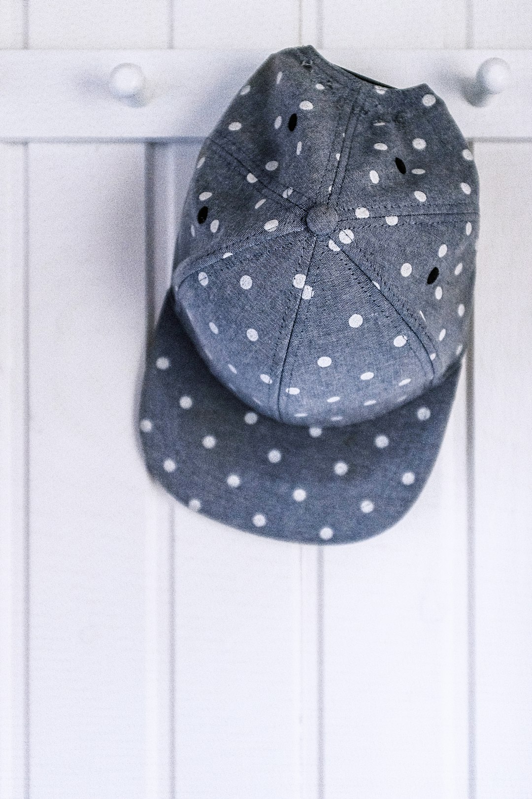 gray and white polka-dot fitted cap on white wooden wall hook