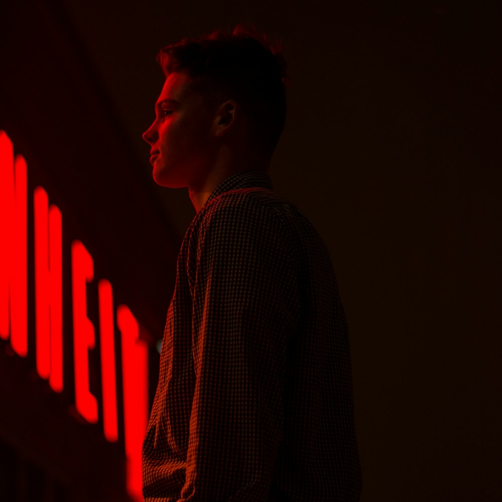 one unknown celebrity in black long-sleeved shirt standing front of neon light signage