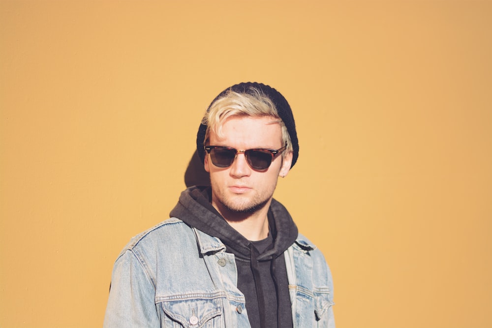 standing man in black framed sunglasses, black beanie cap and blue denim jacket