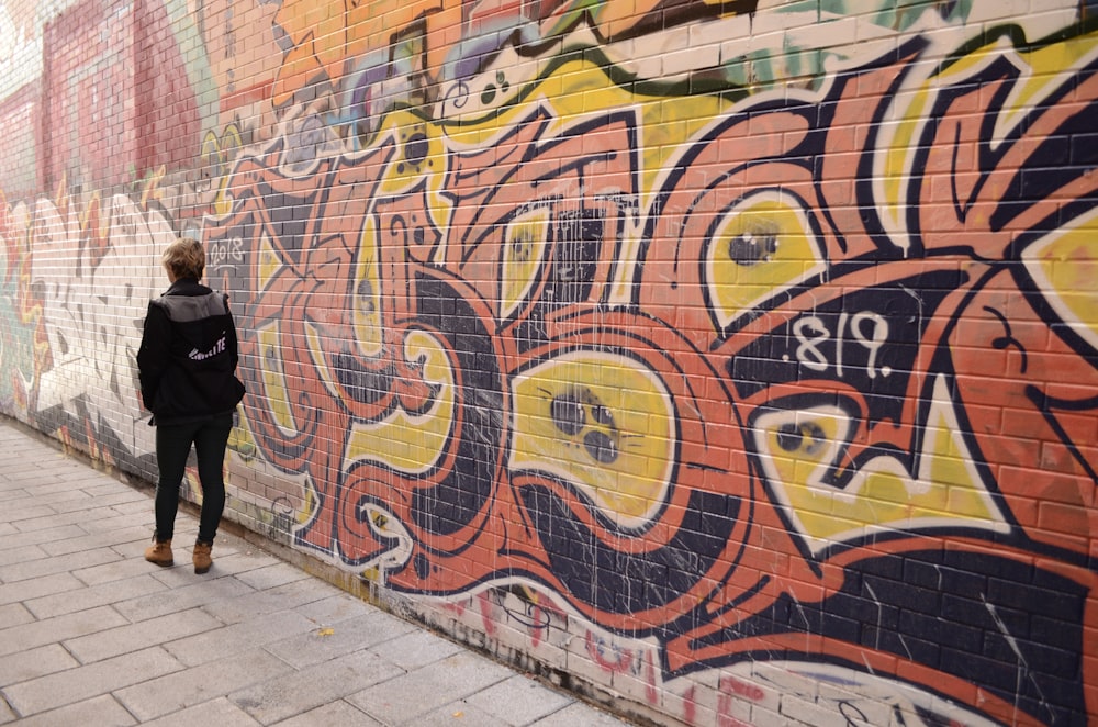 woman walking beside graffiti during daytime