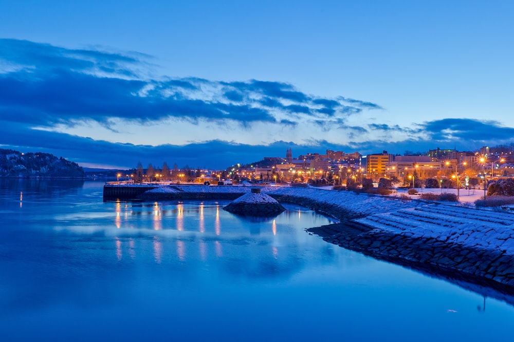 lighted buildings near calm body of water