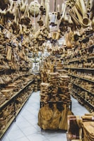 A store filled with numerous wooden items displayed on shelves and hanging from the ceiling. The assortment includes spoons, bowls, cutting boards, and various kitchen utensils made from wood. The arrangement creates a dense and rustic atmosphere.