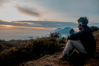 A serene landscape at sunrise with a person meditating on a hilltop, symbolizing reflection and inspiration.