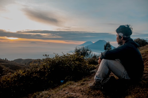 A serene landscape at sunrise with a person meditating on a hilltop, symbolizing reflection and inspiration.