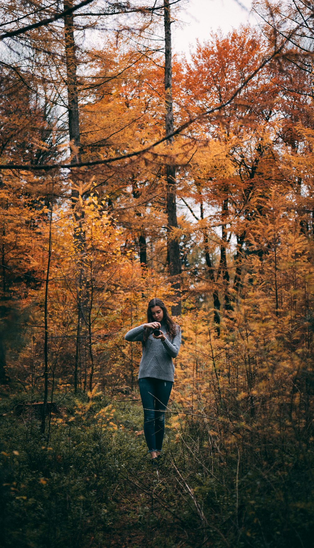woman holding smartphone while standing in front of trees