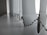 A close-up view of a row of vertical blinds with a bead chain. The blinds are positioned at a window with light filtering through, creating a soft, diffused light effect. The surface appears to be clean and the blinds have a smooth texture.