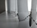 A close-up view of a row of vertical blinds with a bead chain. The blinds are positioned at a window with light filtering through, creating a soft, diffused light effect. The surface appears to be clean and the blinds have a smooth texture.