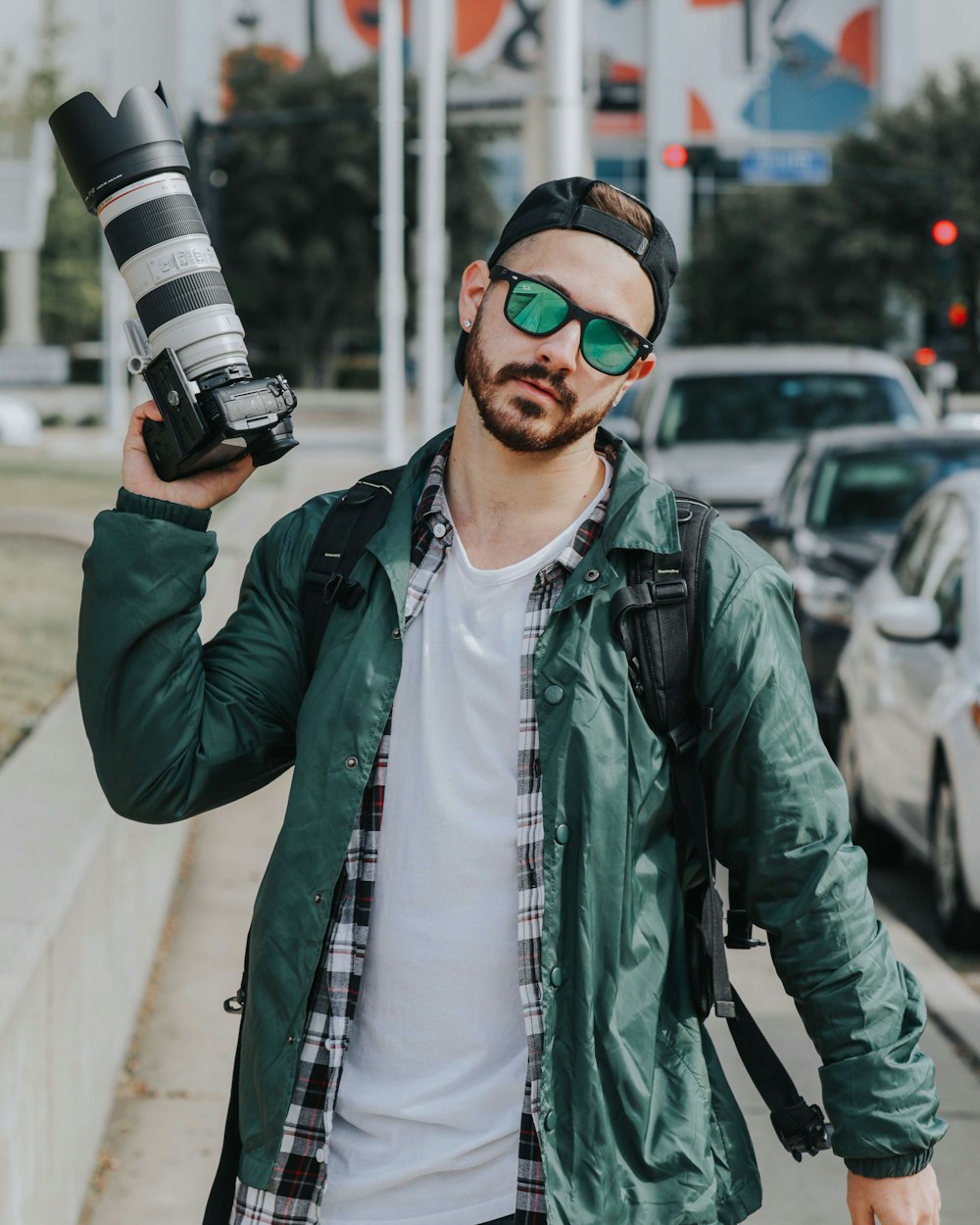 man holding DSLR camera wearing green button-up jacket beside cars