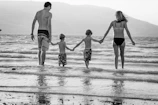 grayscale photography of family walking on beach