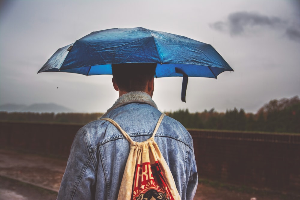 man under blue umbrella with brown drawstring bag